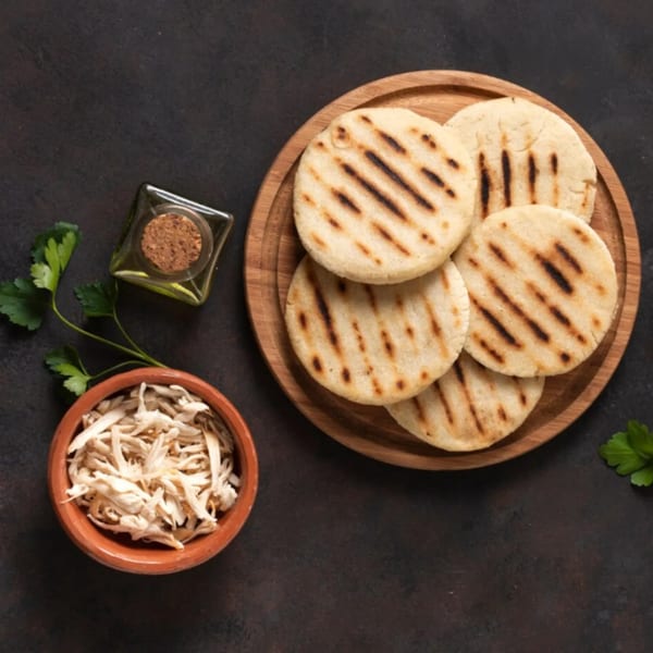 Grilled flatbreads on a wooden plate, with shredded chicken, oil, and parsley on a dark surface.