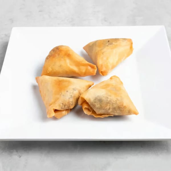 Four golden-brown, triangular Ethiopian sambusas filled with savory ingredients on a white plate.