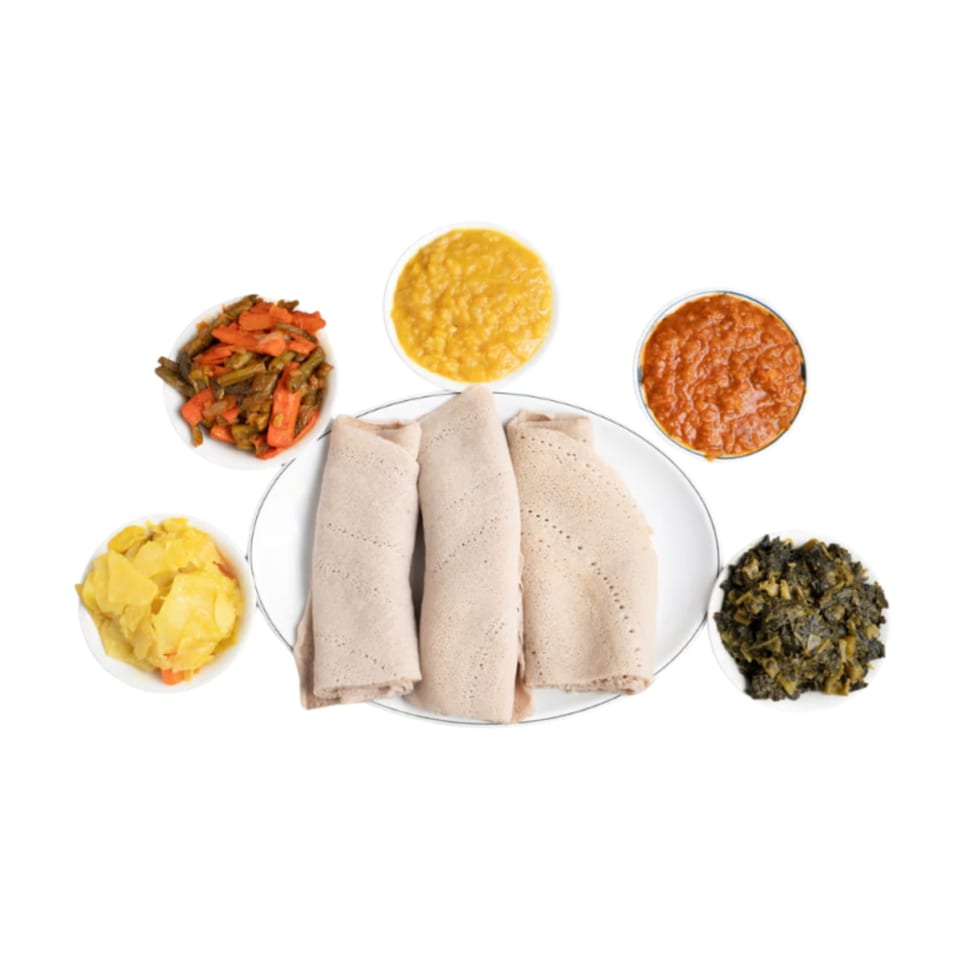 Three injera rolls on a plate surrounded by five bowls of colorful Ethiopian stews and vegetables.