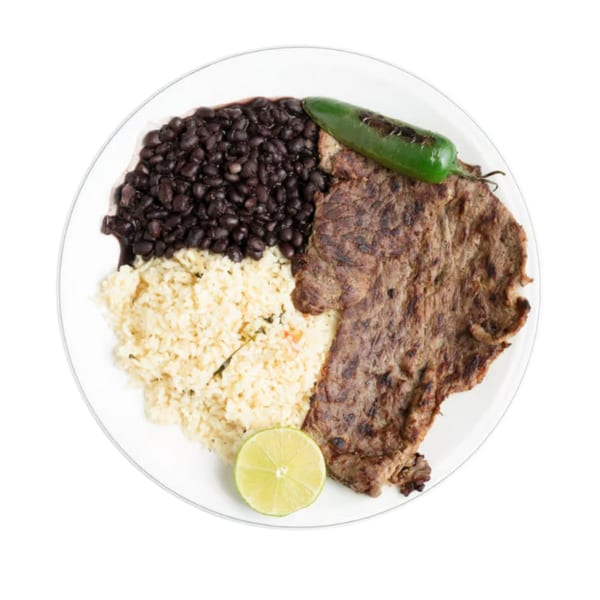 Grilled steak, black beans, rice, a lime wedge, and a charred green pepper on a white plate.